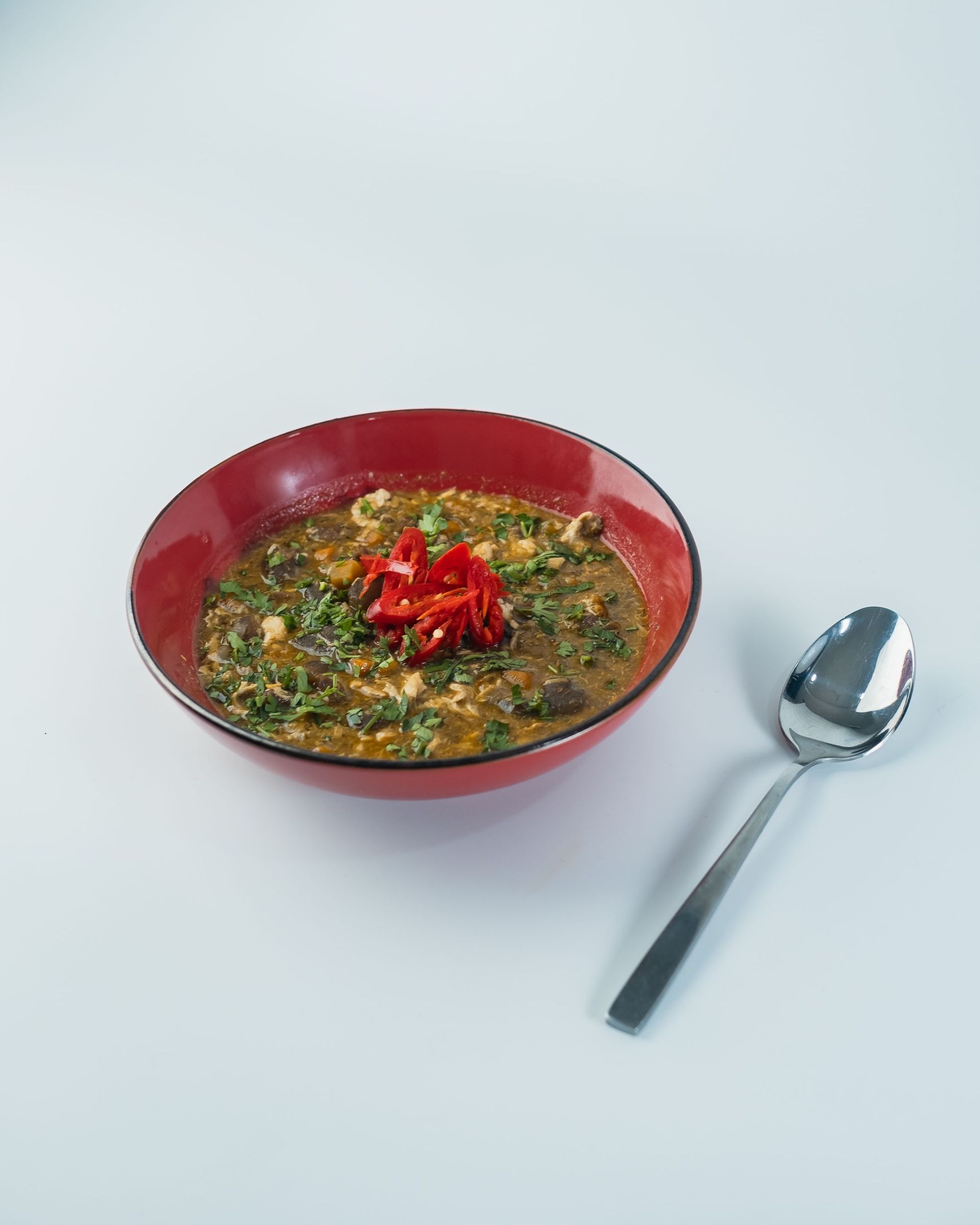 Delicious Nigerian Egusi soup with red peppers and herbs, served in a vibrant red bowl.