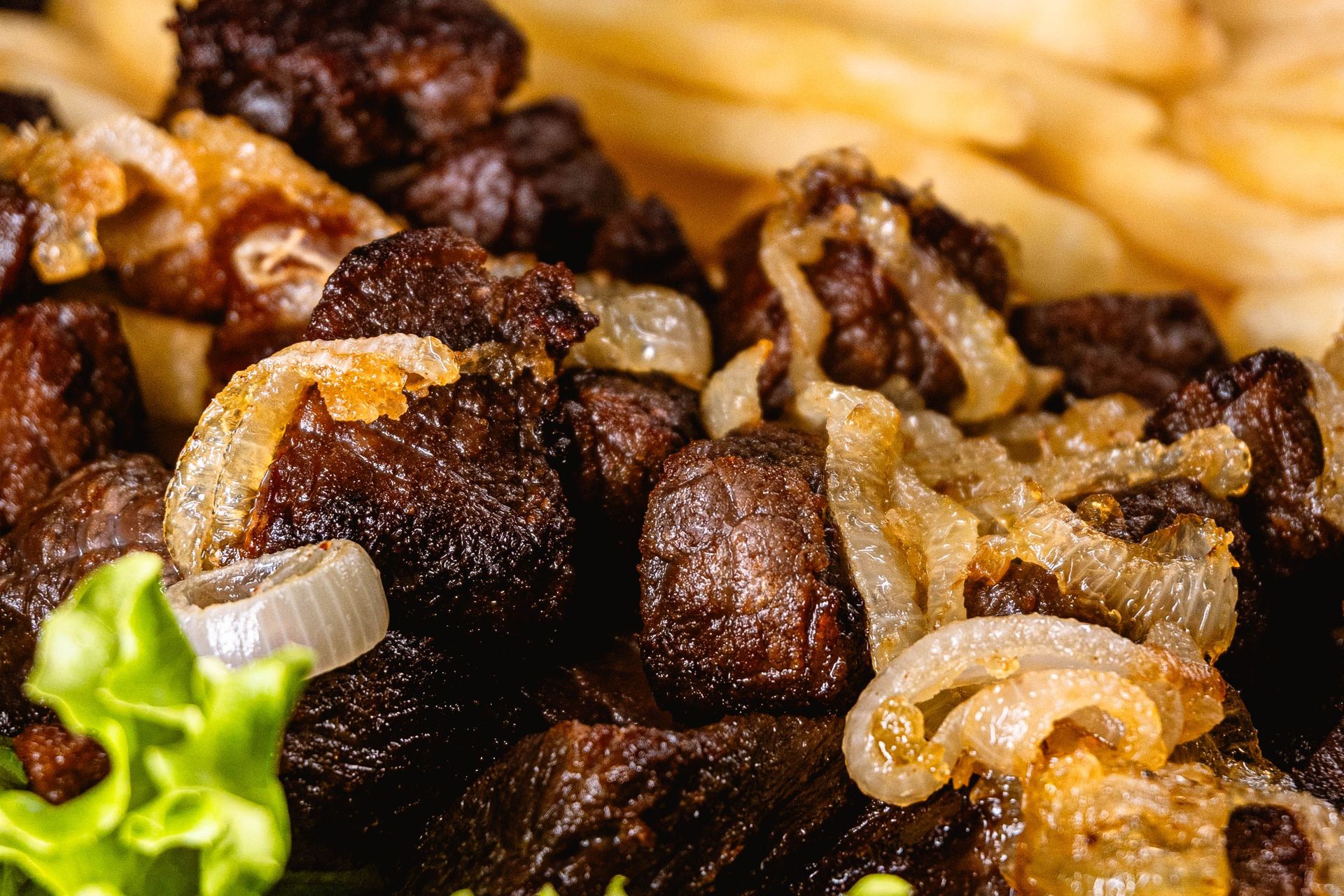 Close-up photo of grilled beef topped with onions, accompanied by fries and lettuce.