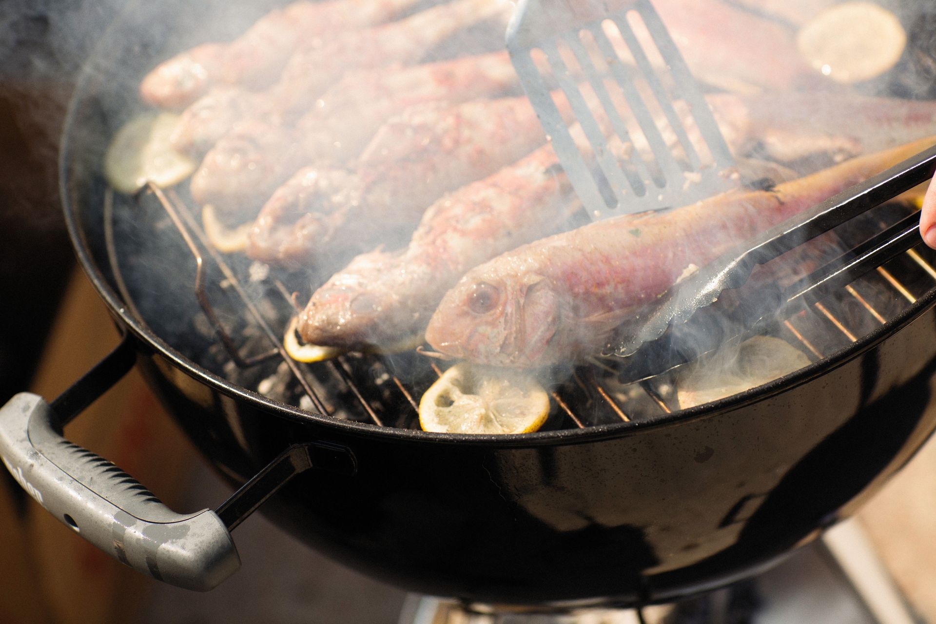 Close-up of red mullets grilling with lemon slices, emitting smoke on a barbecue.