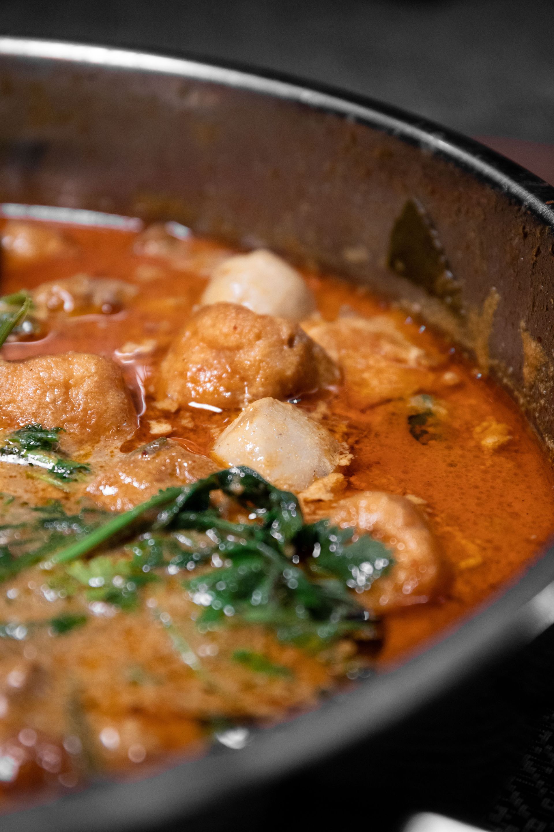 Close-up of a flavorful spicy curry soup with dumplings and fresh greens in a stainless steel pan.