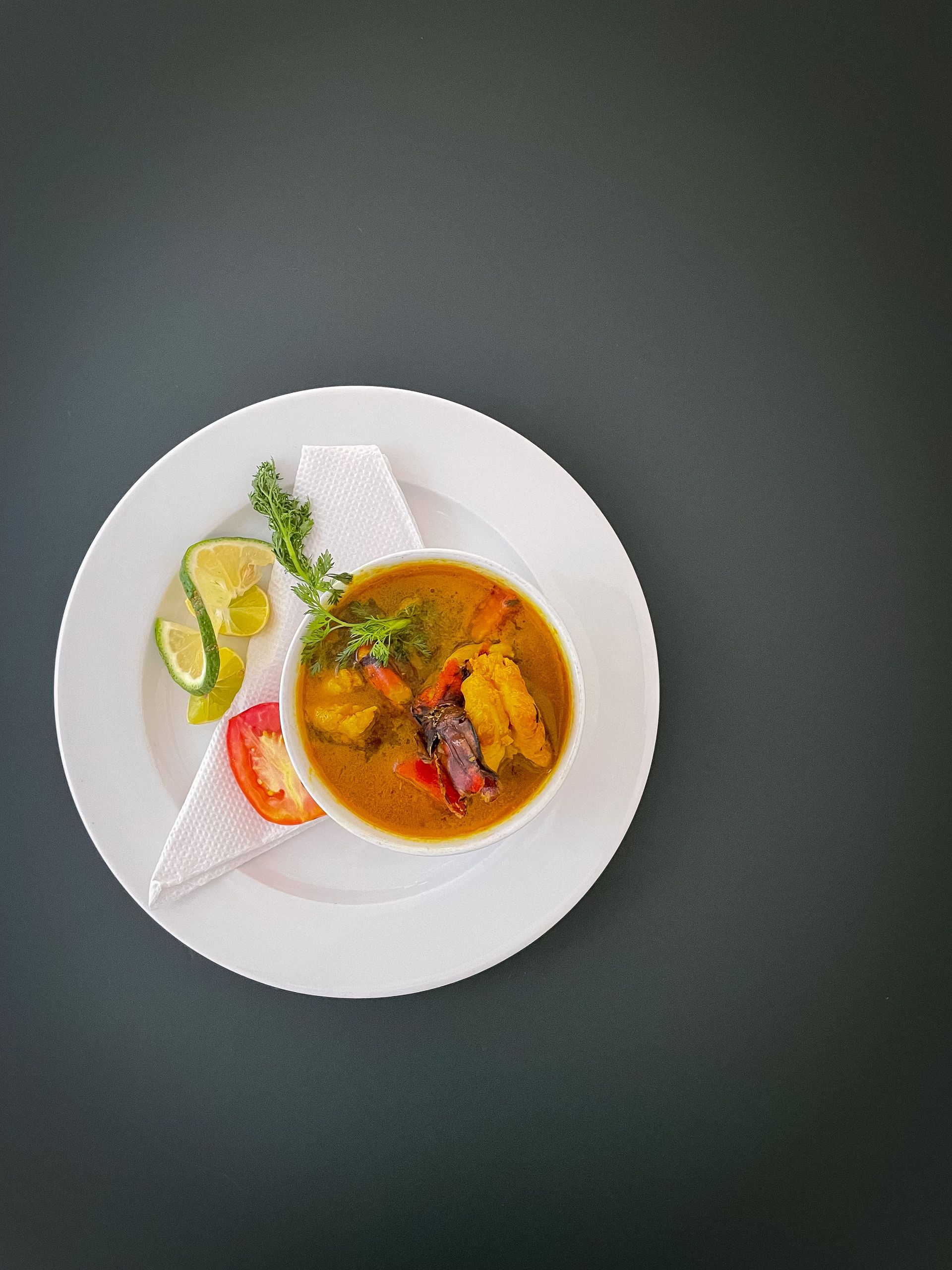 A flavorful bowl of fish soup with herbs and lime, beautifully plated for food photography.